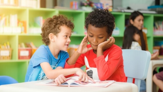 desenvolvimento cognitivo está diretamente ligado ao aprendizado na infância. Na imagem, dois meninos (um negro e um branco) conversam e lêem um livro. Vintage foto criado por tirachard - br.freepik.com