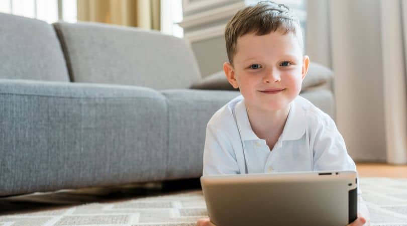 Menino brincando com tablet deitado no tapete da sala da casa dele.